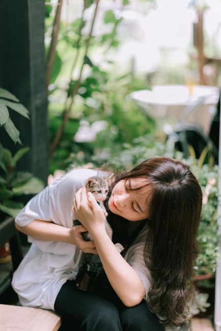 A woman lovingly holds a kitten while sitting in a lush garden, capturing a peaceful moment