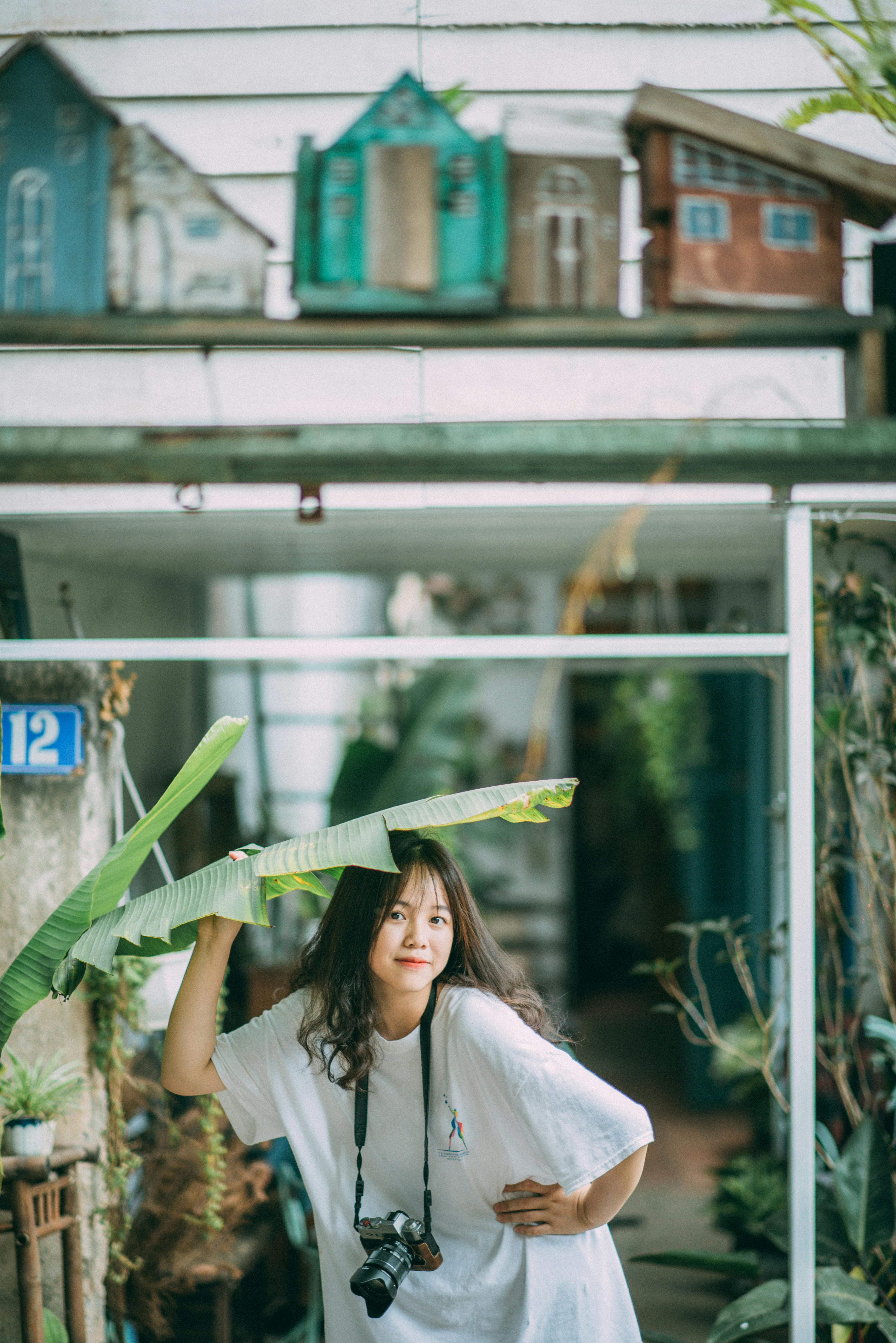 Young woman holding a leaf above her head, outdoors in a vibrant urban setting.
