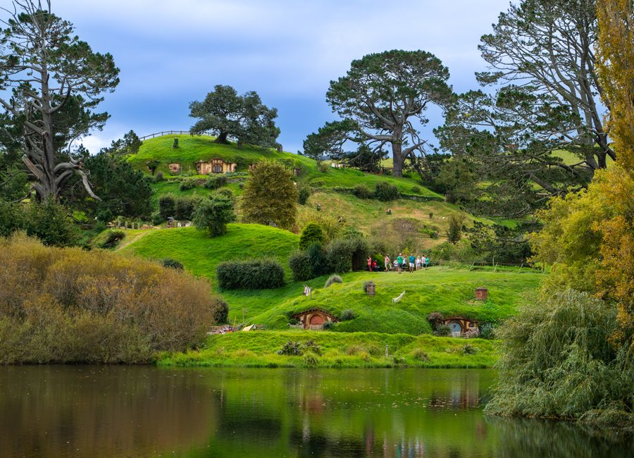 Lush green landscape of Hobbiton with iconic hobbit holes and serene lake reflecting the vibrant scenery.