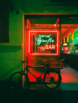 Vibrant neon signage at a bar entrance with a bicycle parked outside, creating a moody urban vibe.