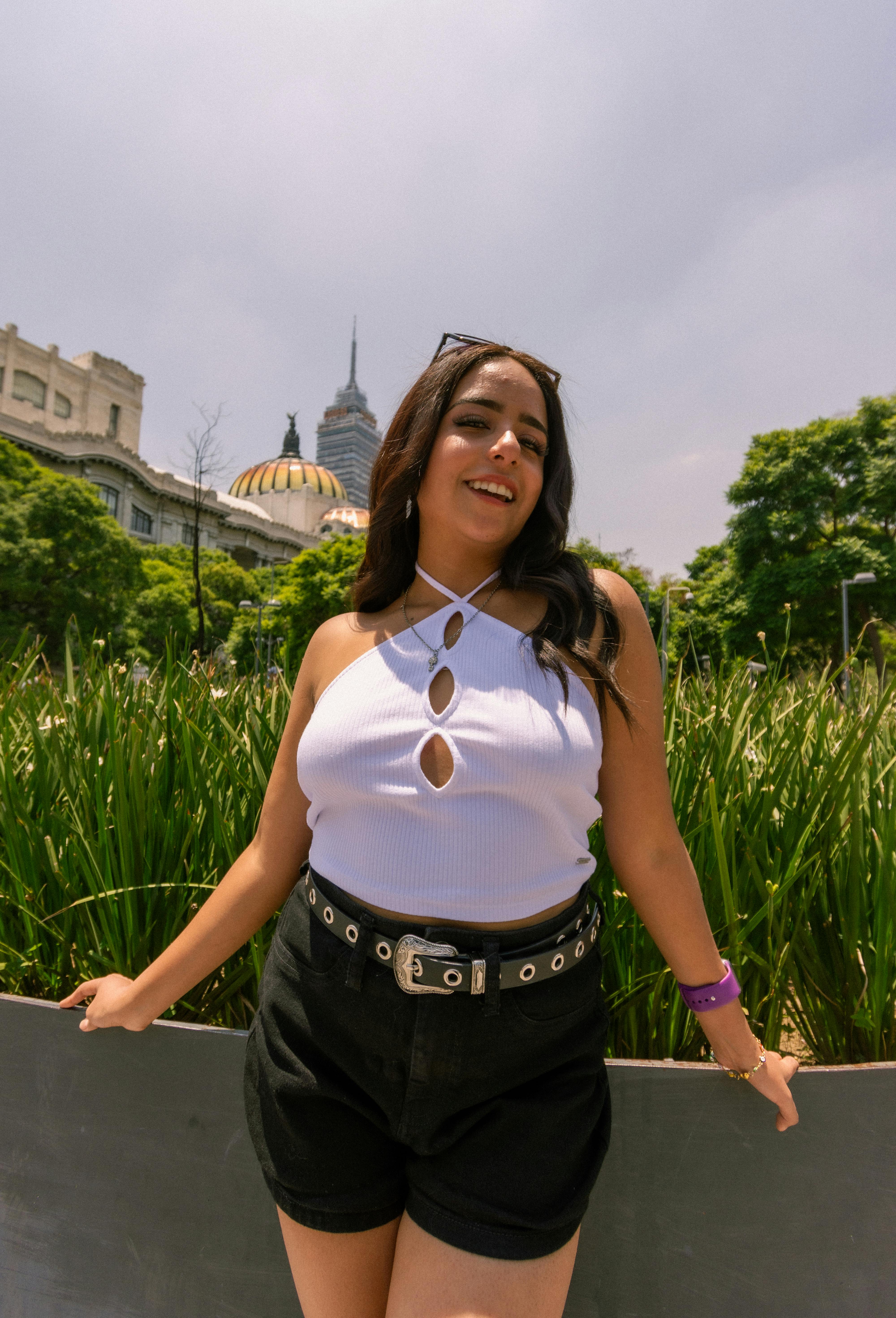 female model wearing a white halterneck and black shorts posing outdoors in summer