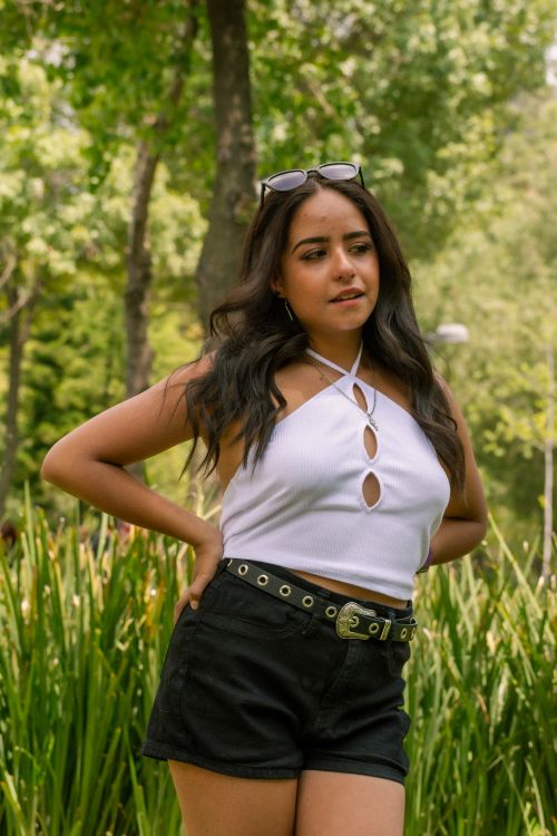 Free Brunette woman in white halterneck and black shorts posing in a park. Stock Photo