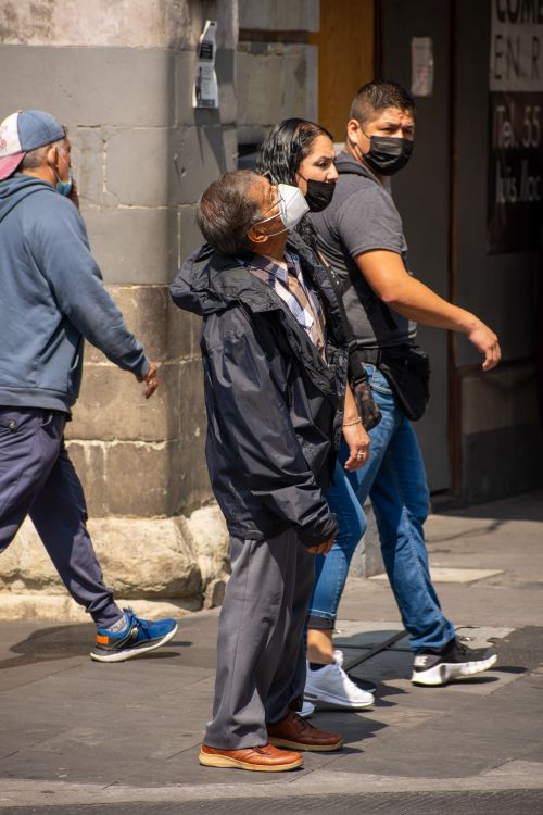 Free A group of people walking on a sunny urban street, all wearing face masks for safety. Stock Photo