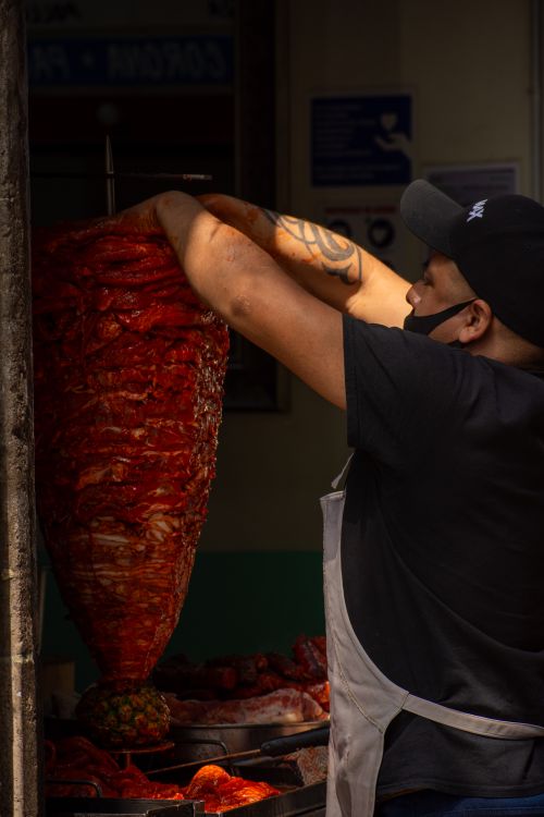 Free Street vendor preparing shawarma on a vertical rotisserie in a bustling city setting. Stock Photo
