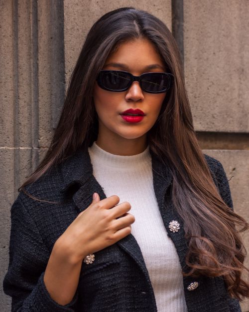 Free Stylish young woman in sunglasses posing in a black blazer against a stone wall. Stock Photo