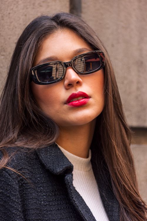 Free Close-up portrait of a young woman wearing sunglasses with an urban backdrop. Stock Photo