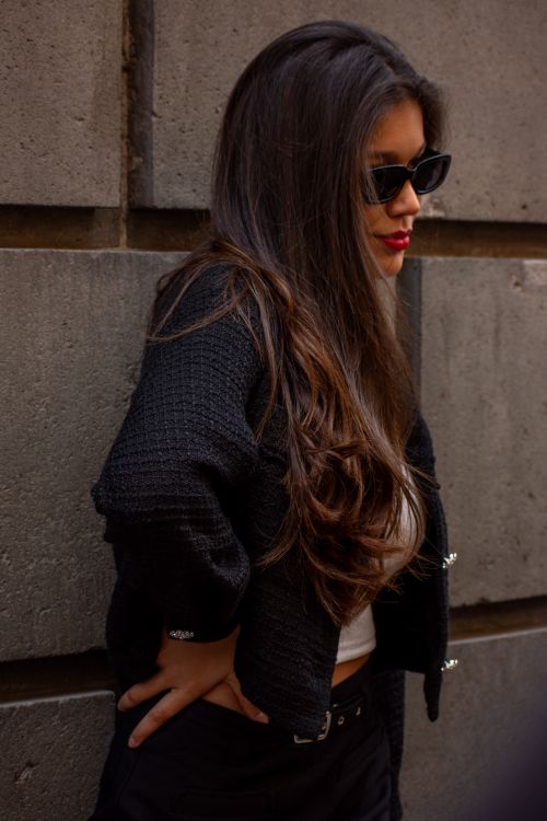 Free Fashionable woman in a black jacket and sunglasses confidently posing against a stone wall. Stock Photo