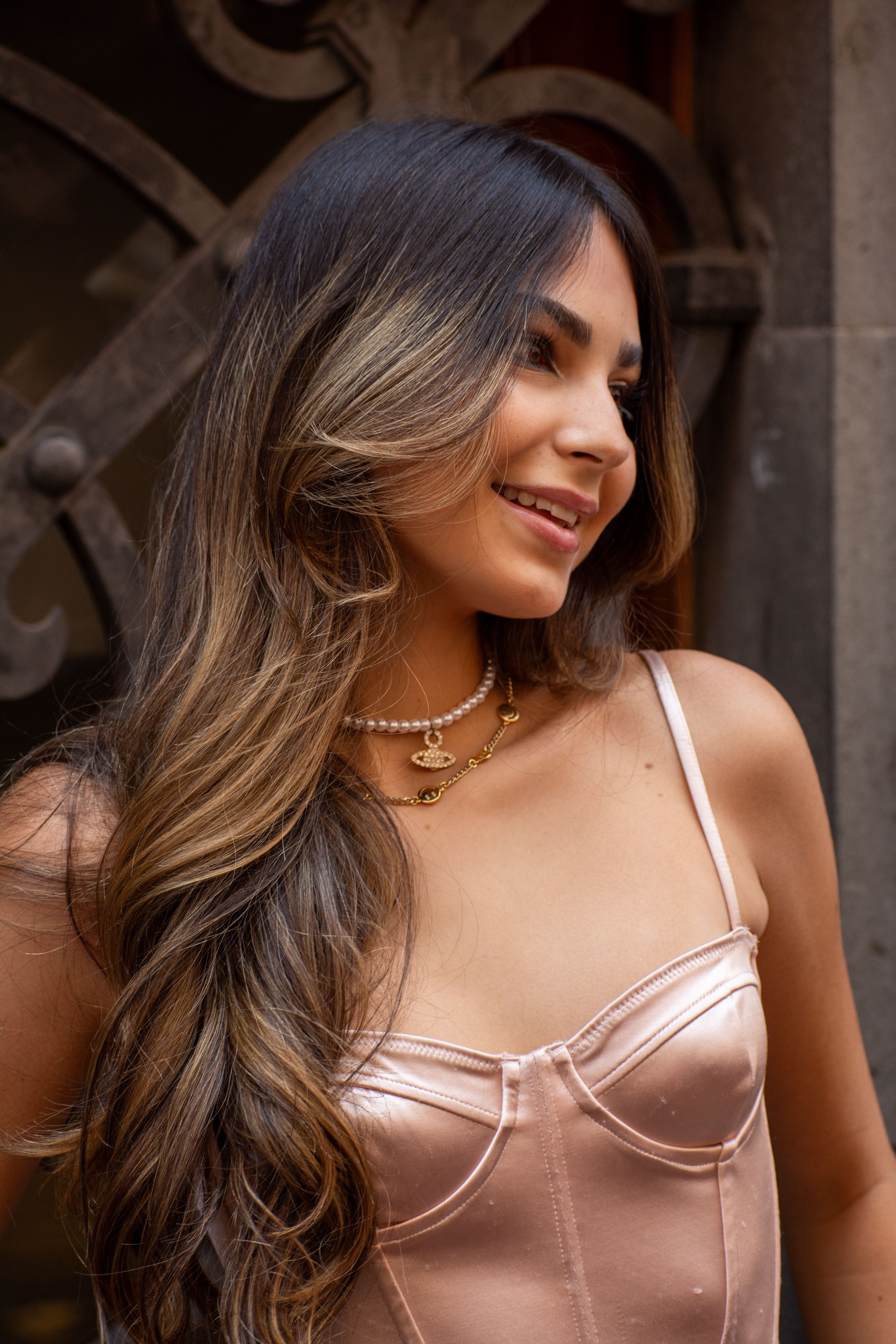 A stylish young woman smiles gracefully outdoors in a satin corset top.