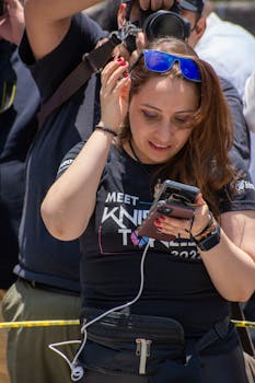 A woman checks her smartphone during an outdoor event, wearing sunglasses.