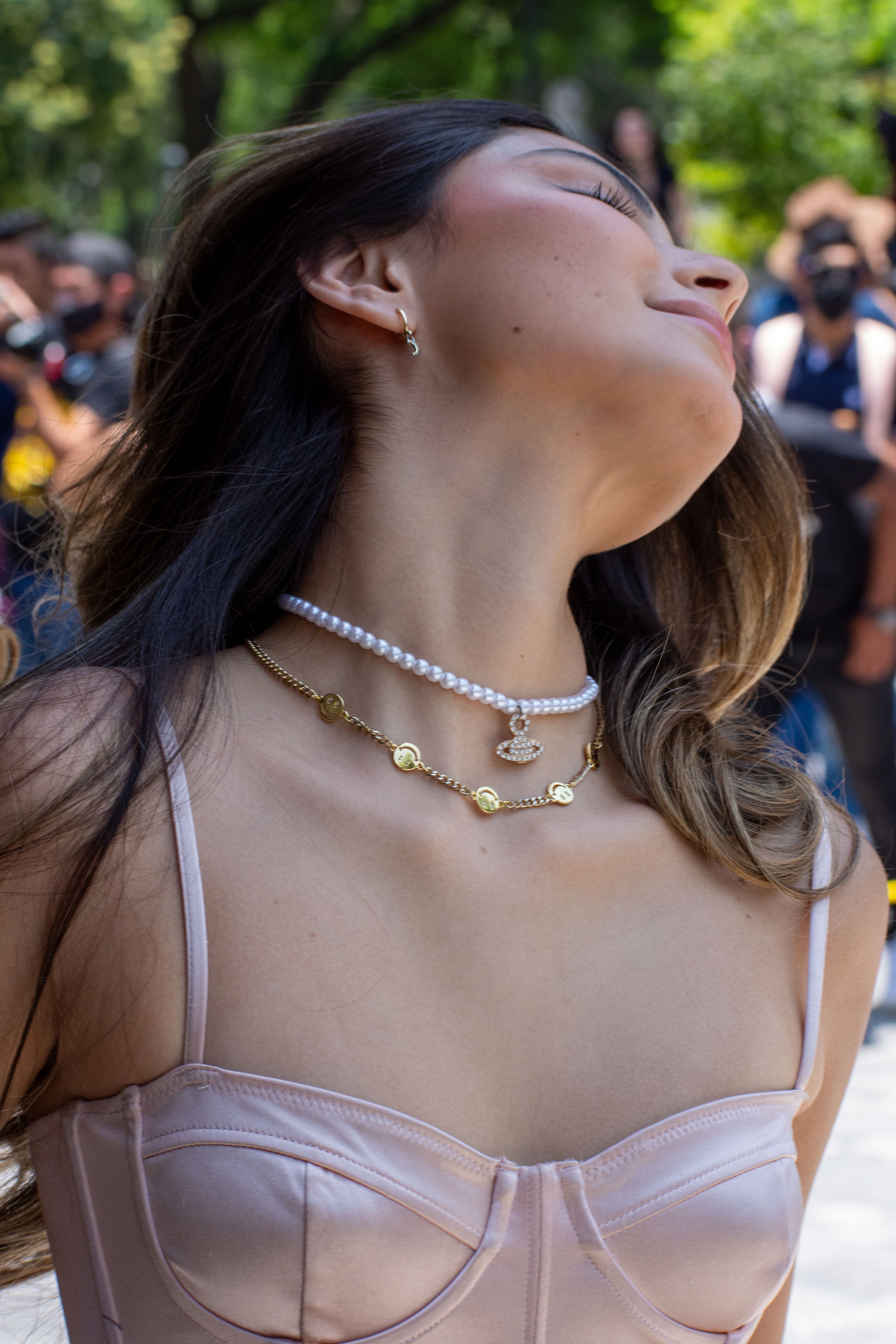 Close-up de uma mulher estilosa usando joias e roupas de moda em um ambiente ao ar livre.
