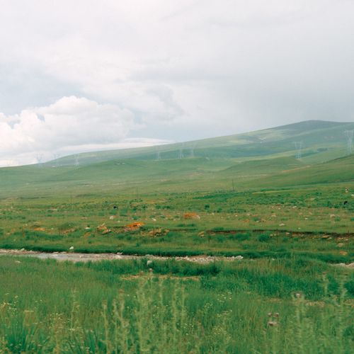 Free Vast landscape view of a green field with hills and transmission towers under a cloudy sky. Stock Photo