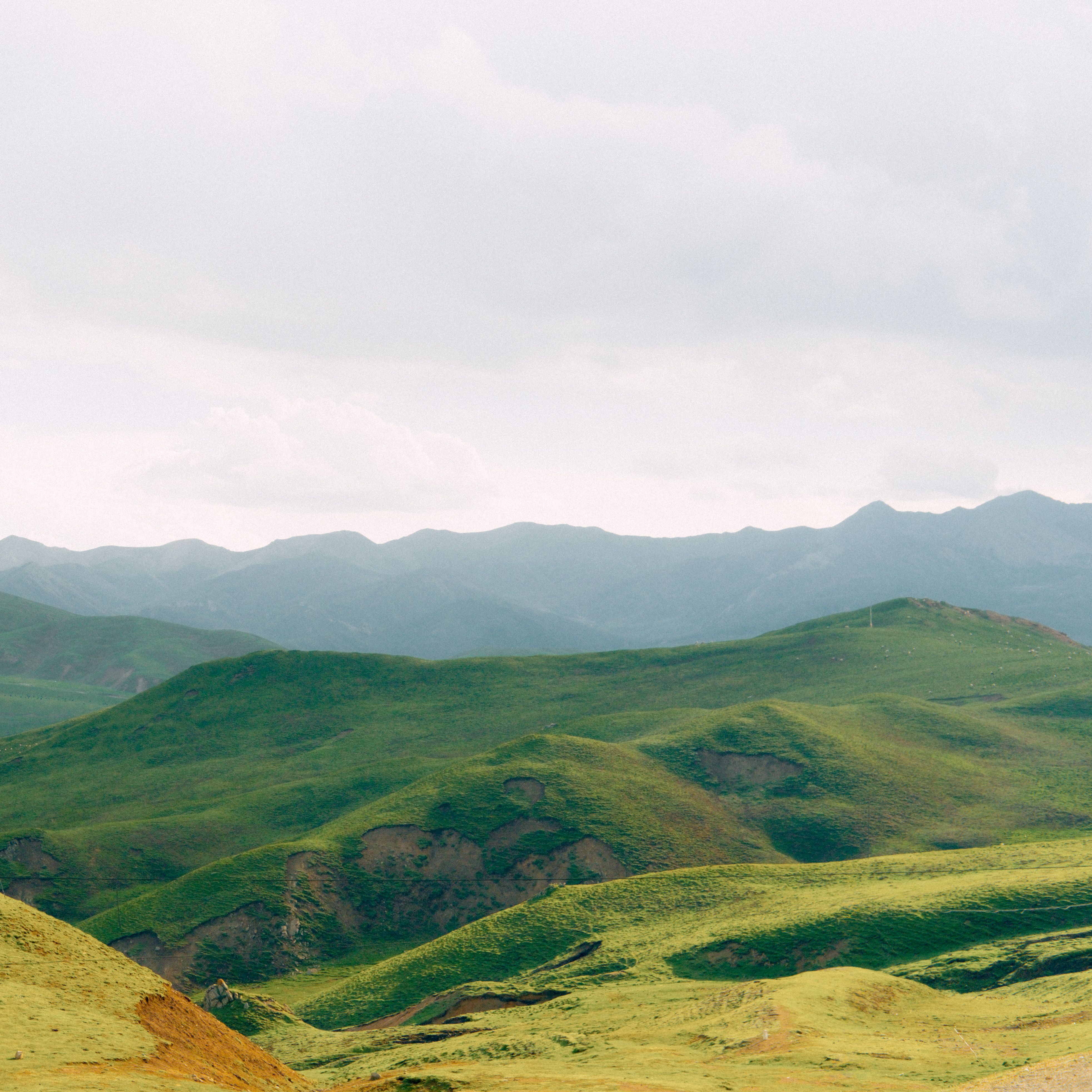 Expansive view of lush green hills and distant mountains under a cloudy sky.