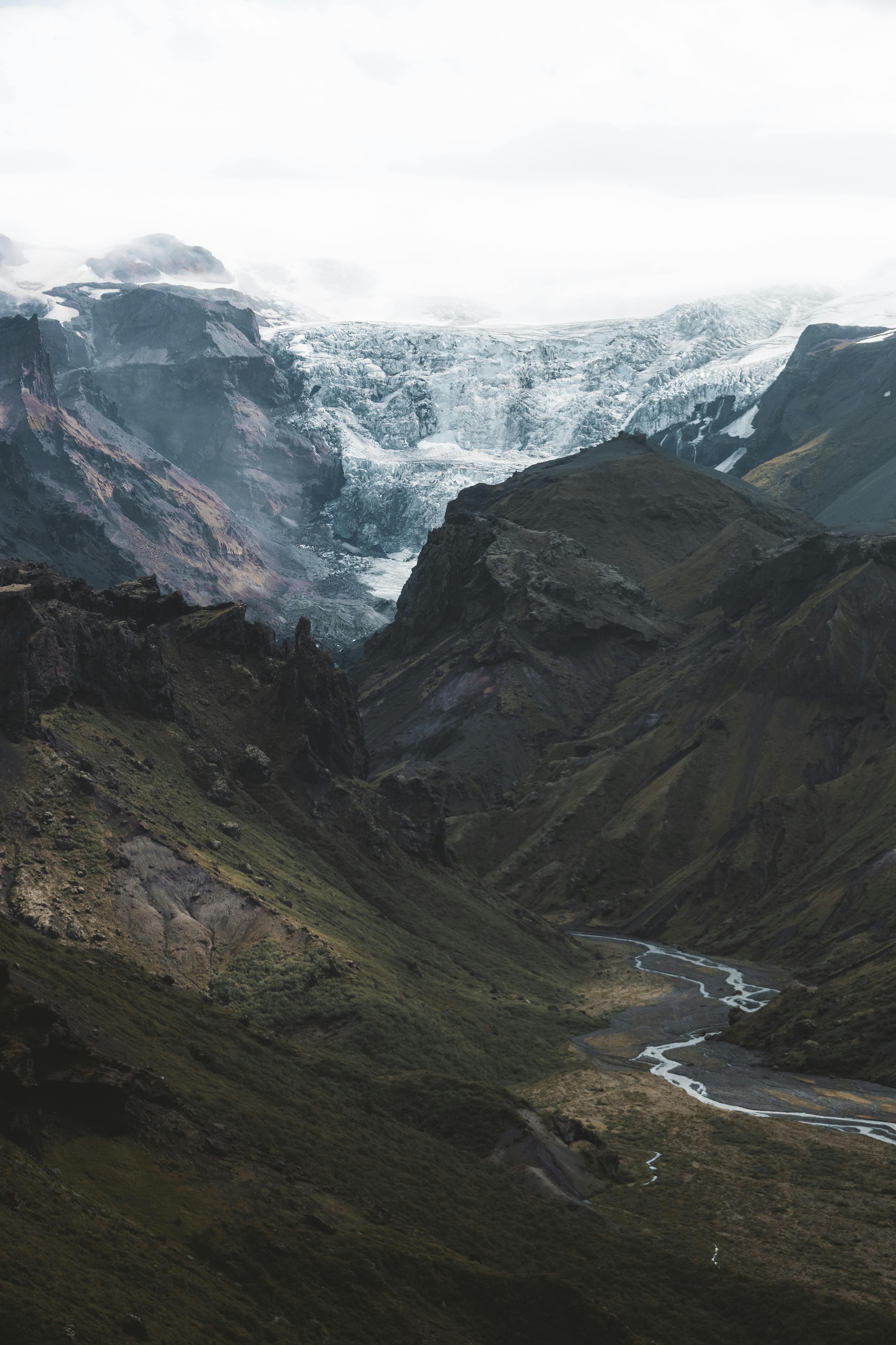Stunning mountain landscape featuring a glacier and winding stream under a cloudy sky.