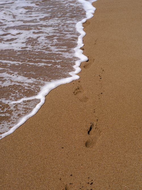 Free Serene sandy beach with footprints leading to gentle ocean waves. Stock Photo