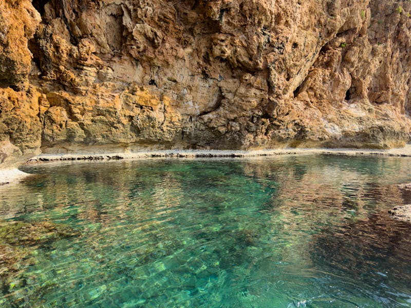 View of turquoise Mediterranean water meeting rough cliff surface at a natural swimming spot