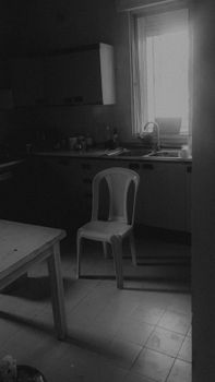 A grayscale photo of a simple kitchen with a plastic chair and table.