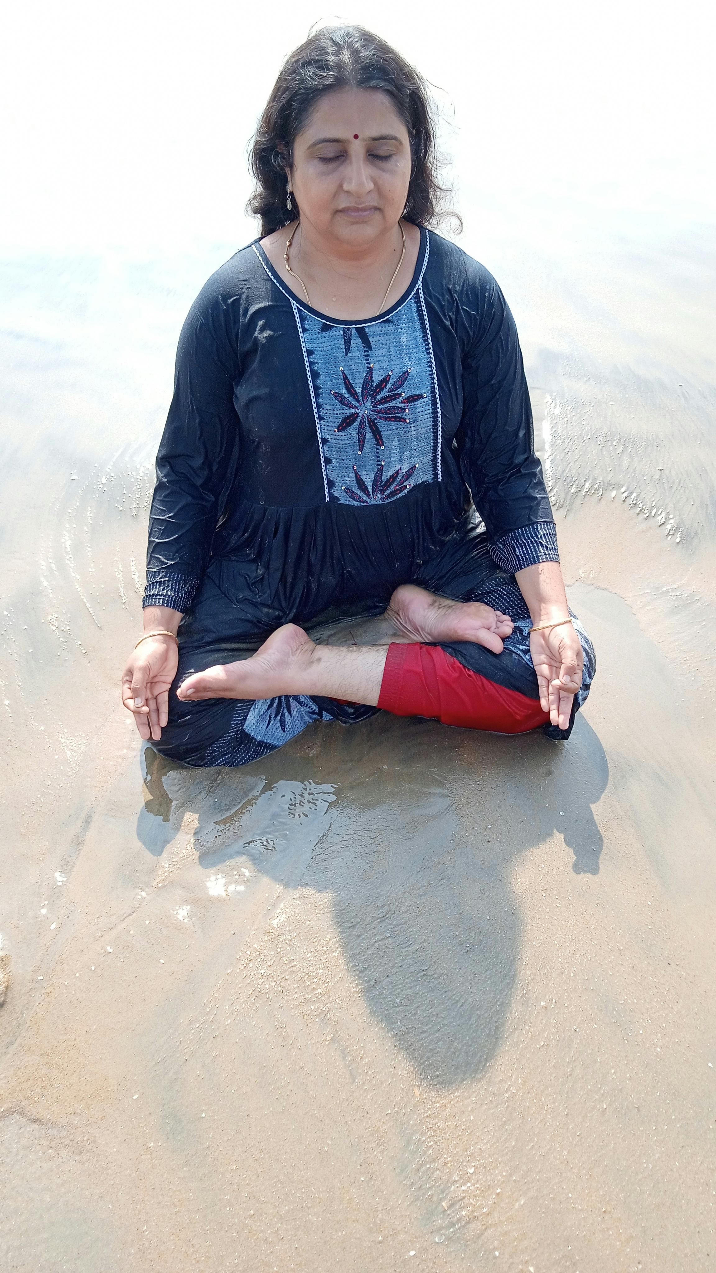 South Asian woman meditating on the sandy beach of Chennai, India, in a serene setting.