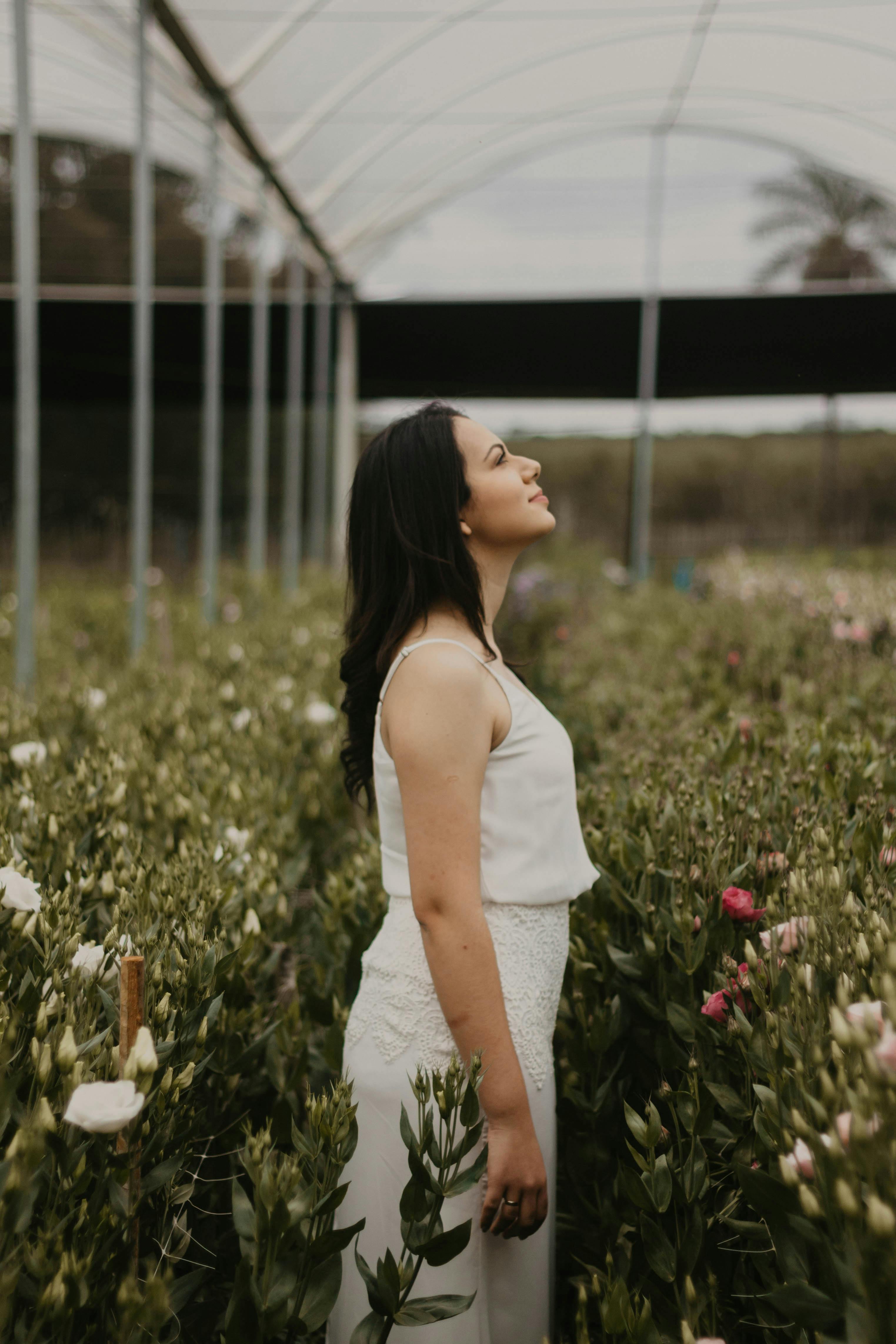 Young woman standing in a São Paulo greenhouse surrounded by lush flowers, gazing upward.