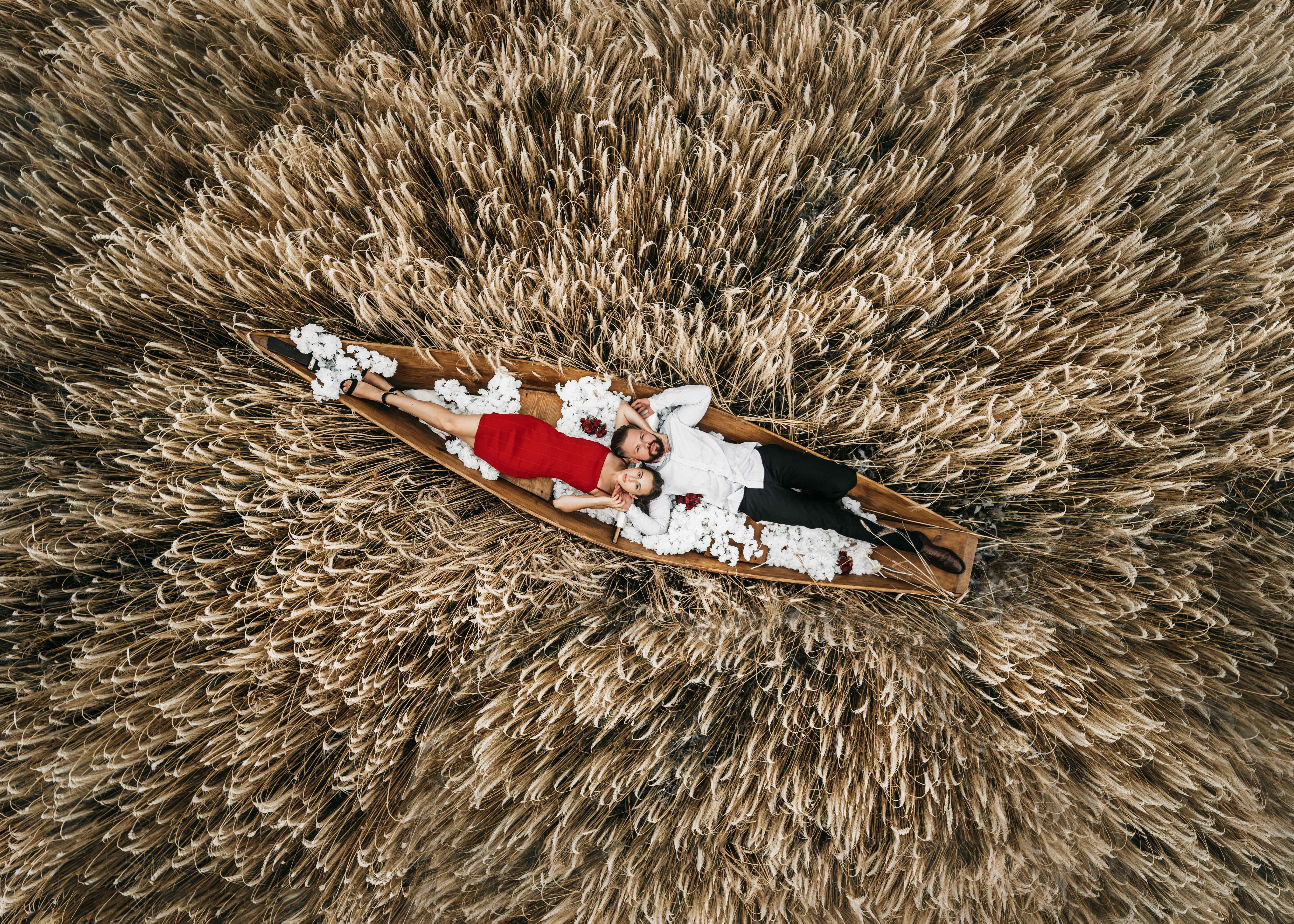 Aerial view of a couple lying in a canoe amid a serene wheat field. Perfect harmony.