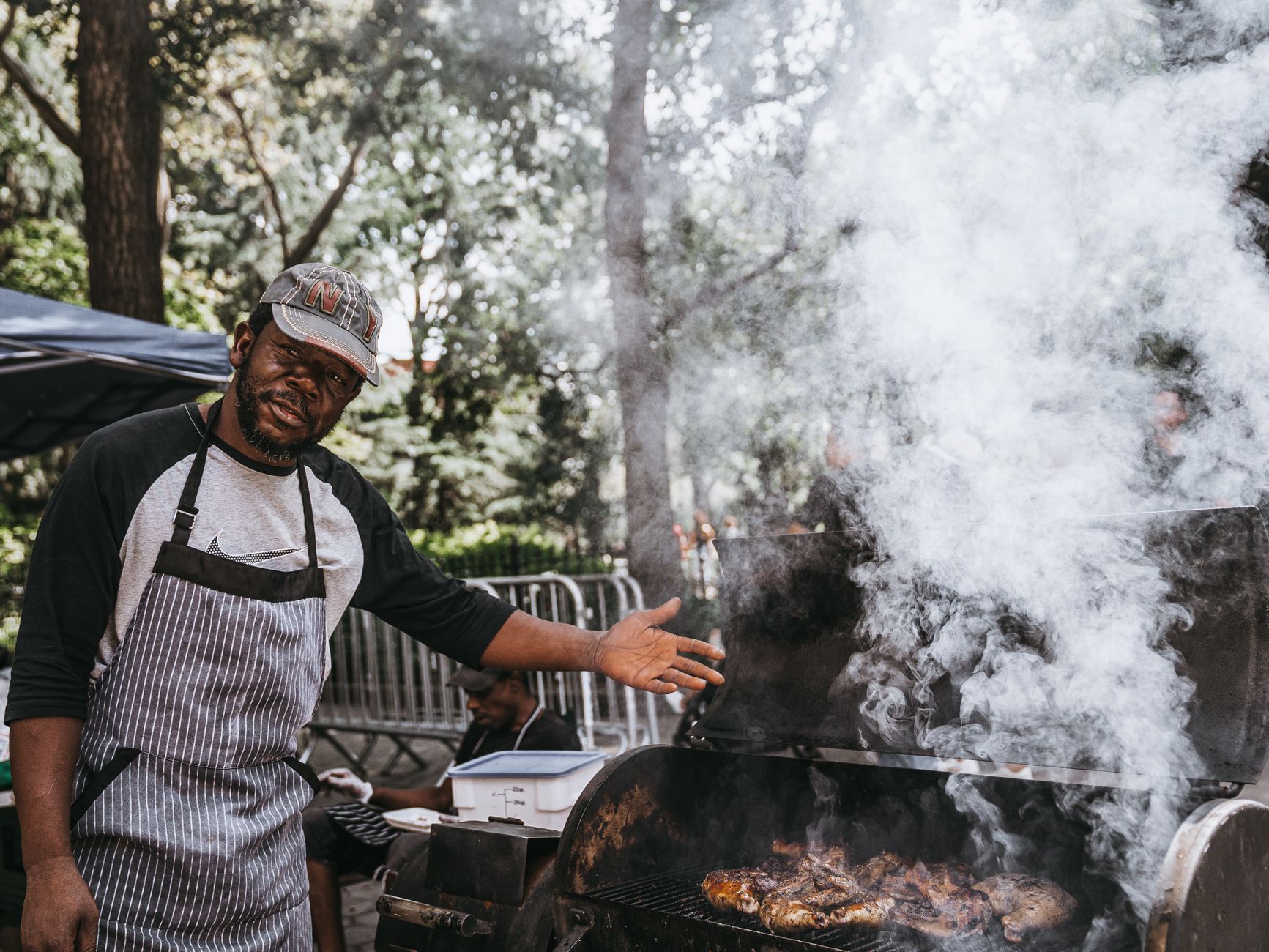 A man grilling meat outdoors with smoke rising from the barbecue.