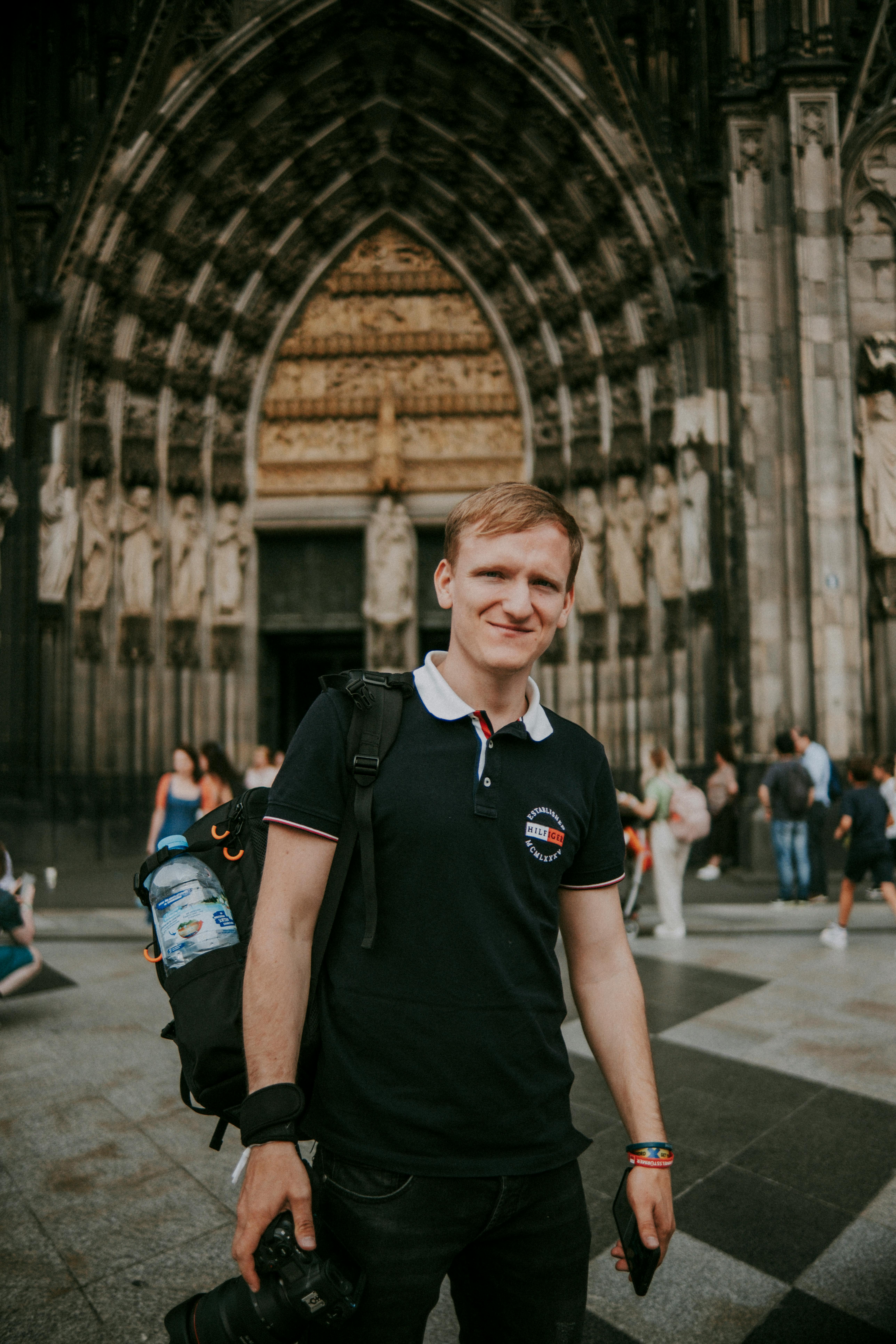 A young man smiles in front of a grand cathedral, radiating travel vibes.