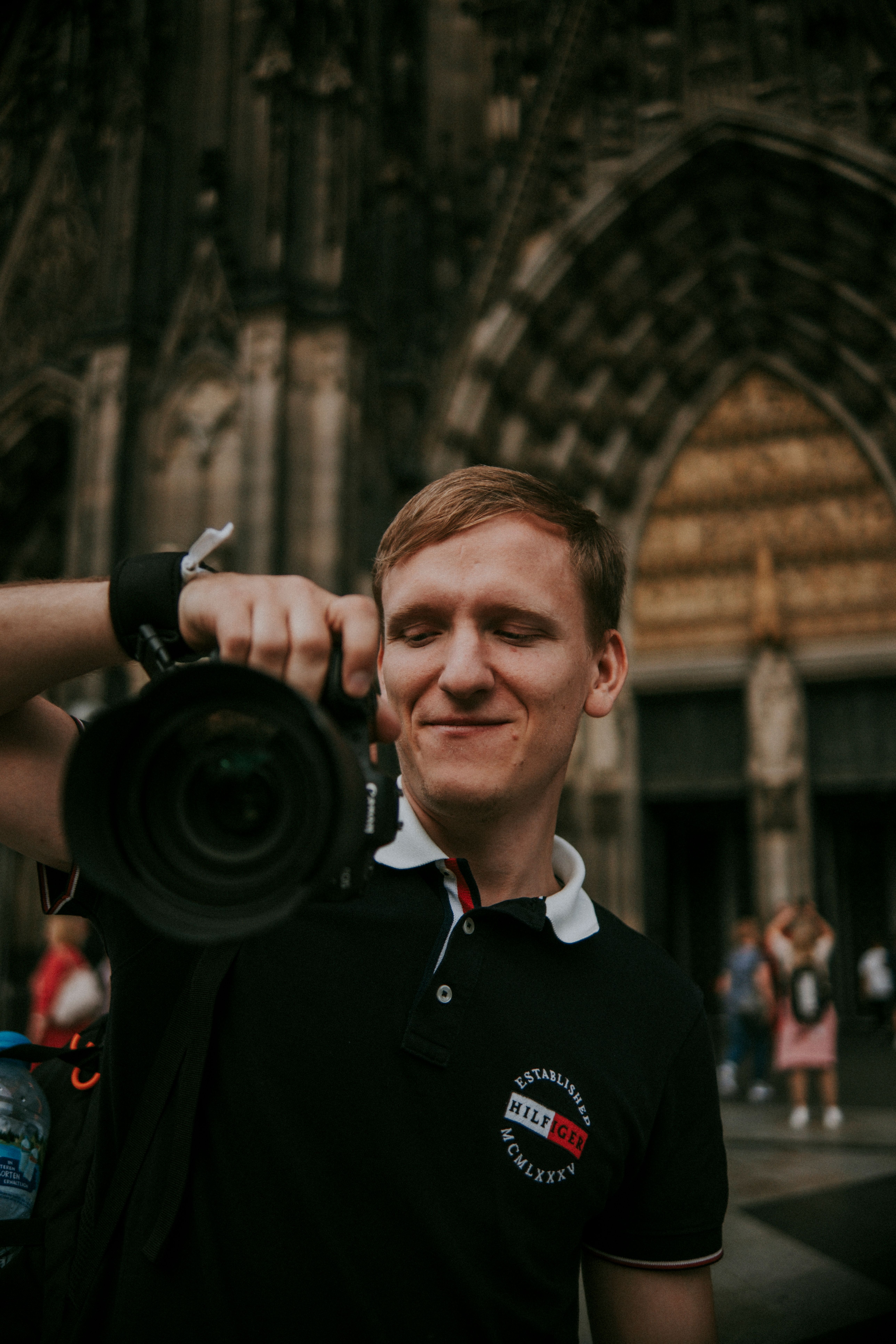A photographer smiles while holding a camera in front of a grand cathedral facade.