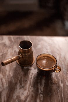 Turkish coffee in a copper pot and cup on a marble table, showcasing traditional coffee culture.