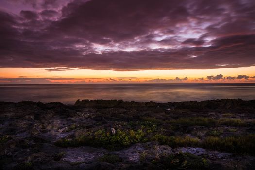 Breathtaking sunset over the rocky seashore of Akumal, Mexico with vibrant colors and dramatic clouds.