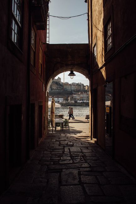 Charming alleyway in Porto, Portugal opening up to the scenic Douro River view. Captures urban architecture under soft daylight.