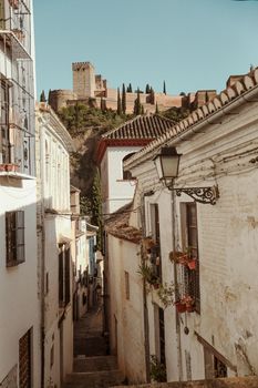 Charming alley in Granada with a view of the majestic Alhambra castle under a clear blue sky.