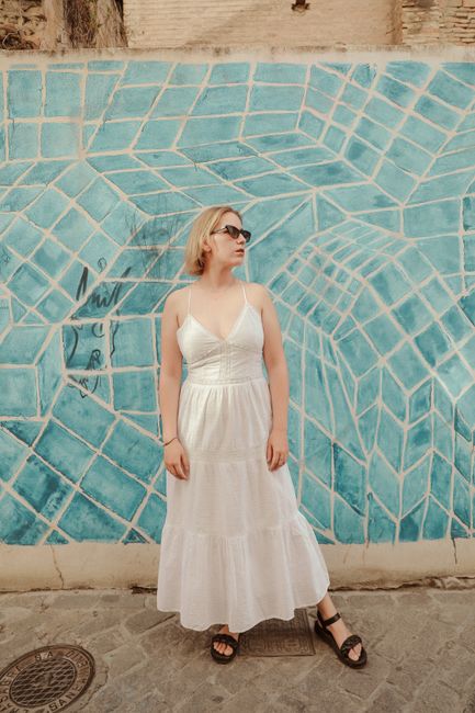 Woman in white dress poses against a vibrant blue geometric wall in an urban setting, exuding style and confidence.