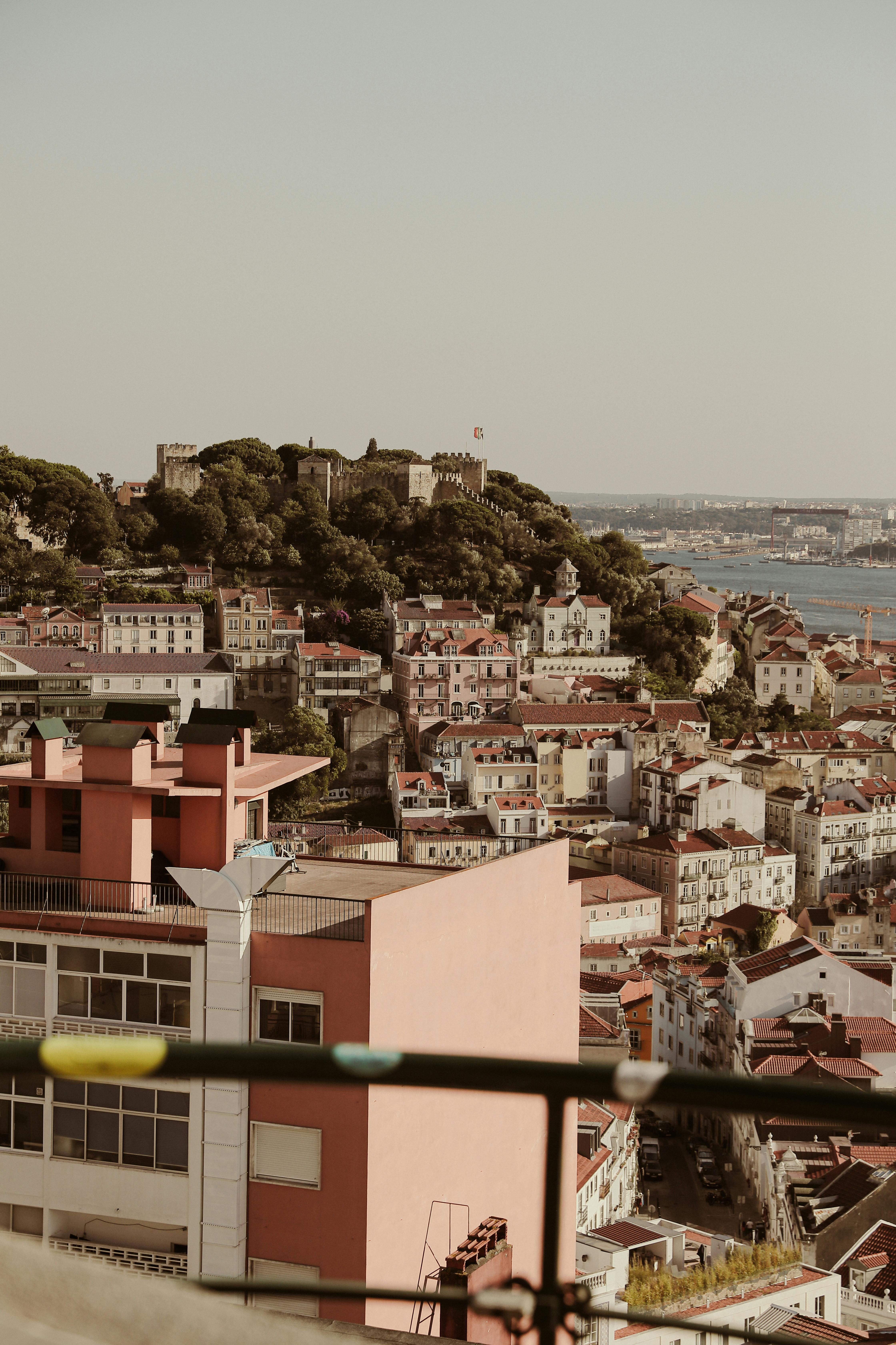 Scenic aerial view of Lisbon cityscape with historic castle, rooftops, and river backdrop.