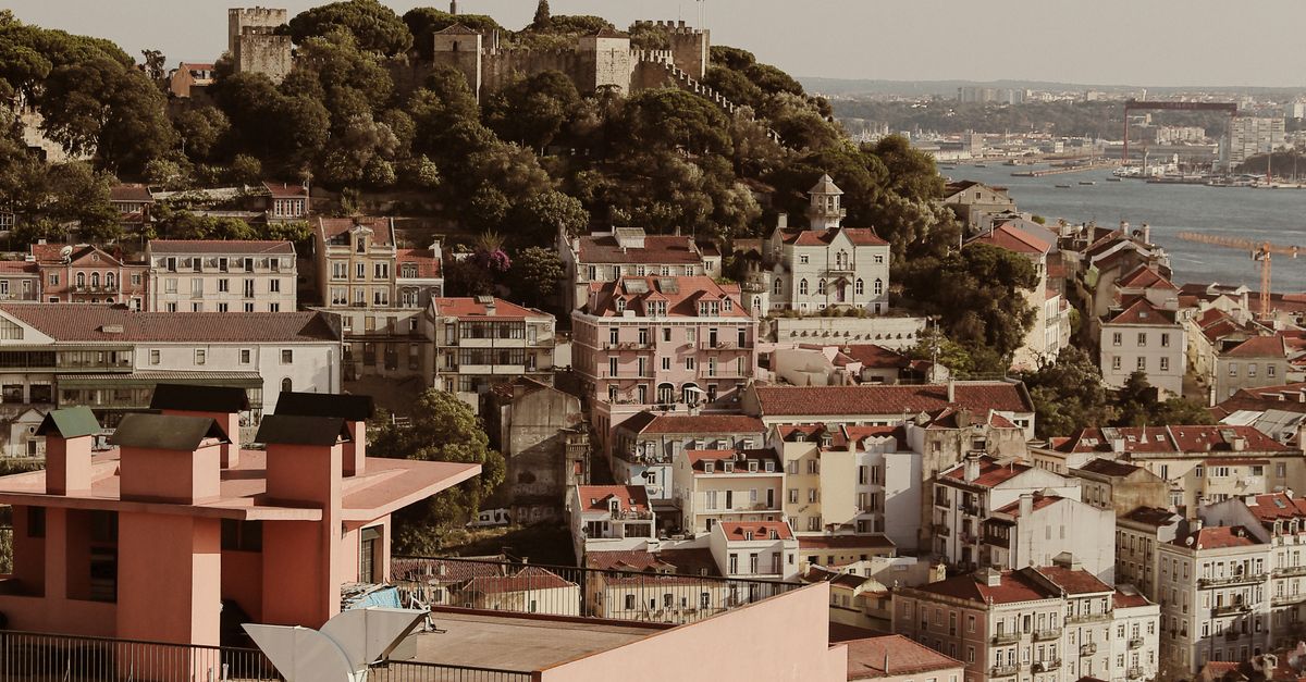 Scenic aerial view of Lisbon cityscape with historic castle, rooftops, and river backdrop.