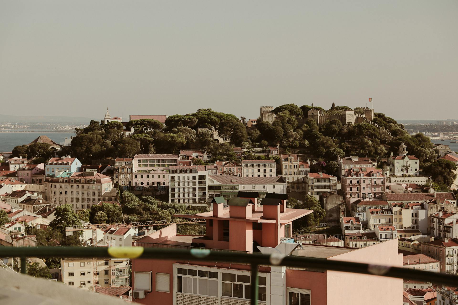 A picturesque panorama of Lisbon cityscape highlighting Saint George's Castle with lush greenery on a hilltop.