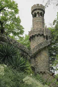 Stone tower surrounded by lush greenery in Sintra's Quinta da Regaleira, Portugal.