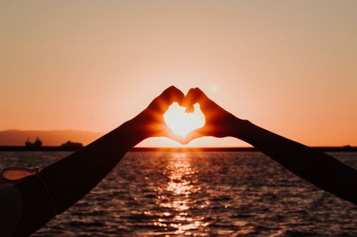 Free A romantic silhouette of hands forming a heart shape with the sun setting over İzmir's sea. Stock Photo