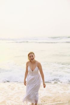 A smiling woman in a white dress stands by the sea, capturing a joyful beach moment.