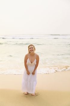 A smiling woman in a white dress enjoying the beach during a sunny day.