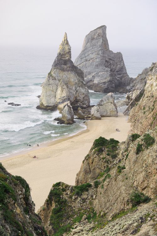 Free Stunning view of towering cliffs and a tranquil sandy beach with ocean waves. Stock Photo