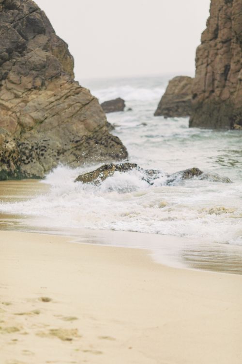 Free Calm beach scene with gentle waves crashing against rocky formations under an overcast sky. Stock Photo
