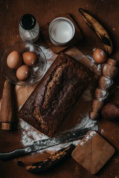 Top view of homemade banana bread with eggs, milk, and baking ingredients on a rustic table.