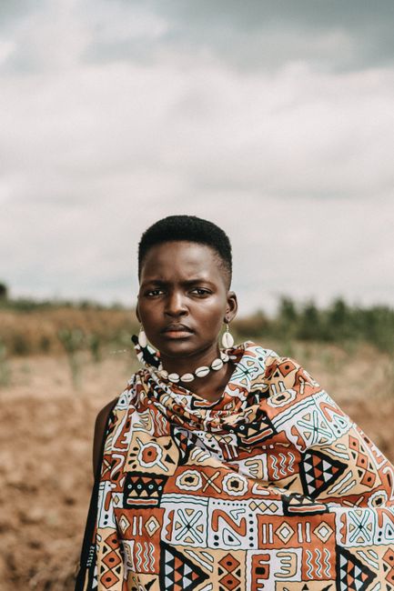Young African woman in vibrant traditional clothing and jewelry, outdoors.