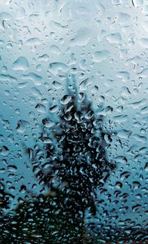 Artistic close-up of raindrops on a window, capturing a blurred tree silhouette.