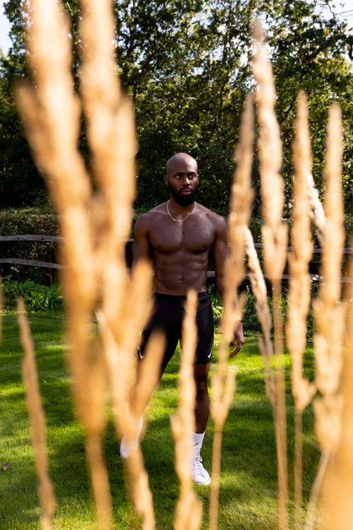 Free Shirtless athletic man posing in grassy yard under sunlight, emphasizing fitness and strength. Stock Photo