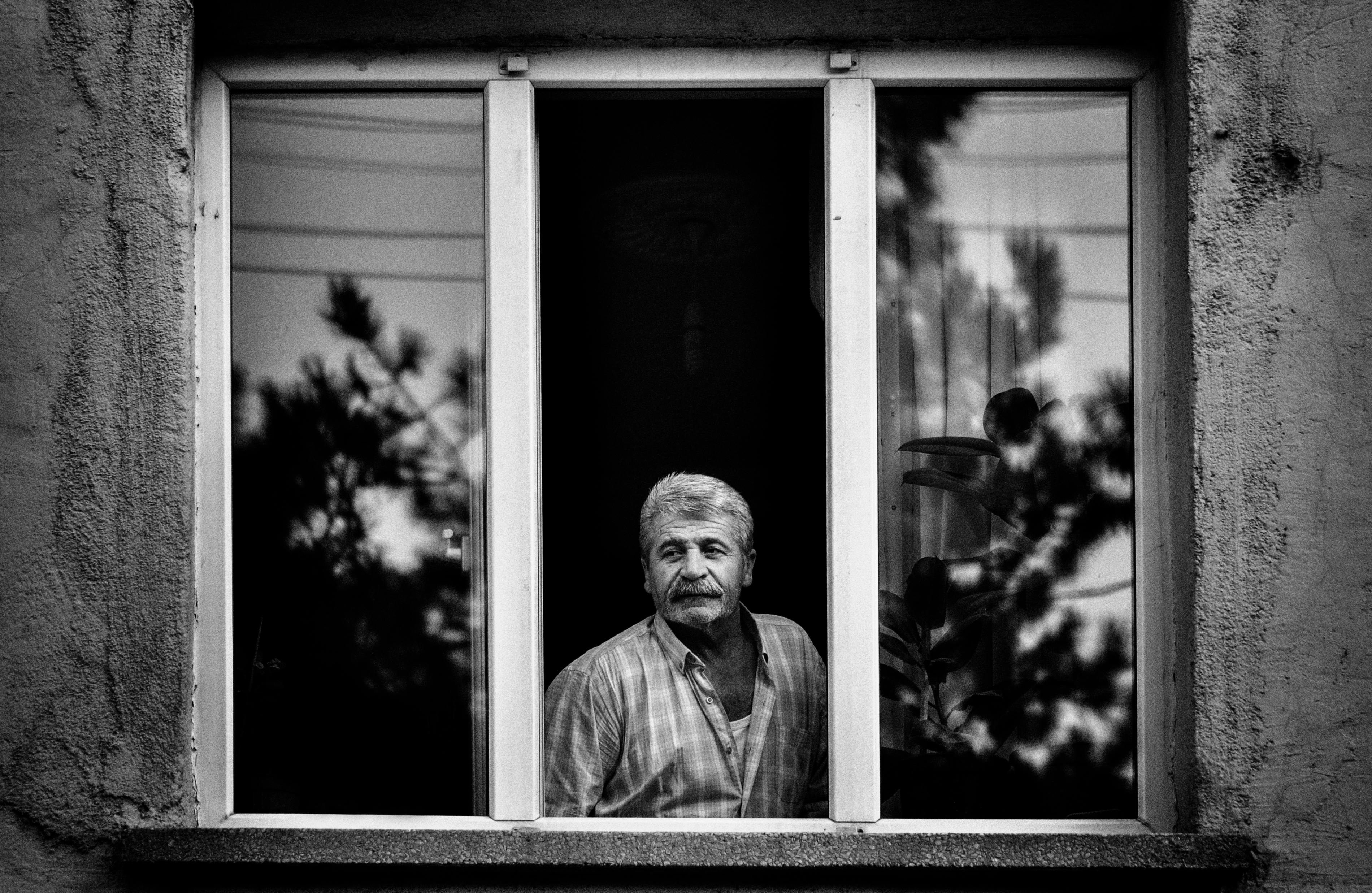 Elderly man with a mustache looking through a window in black and white.