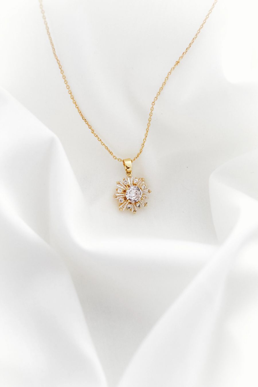 Gold necklace with a delicate pendant on soft white fabric