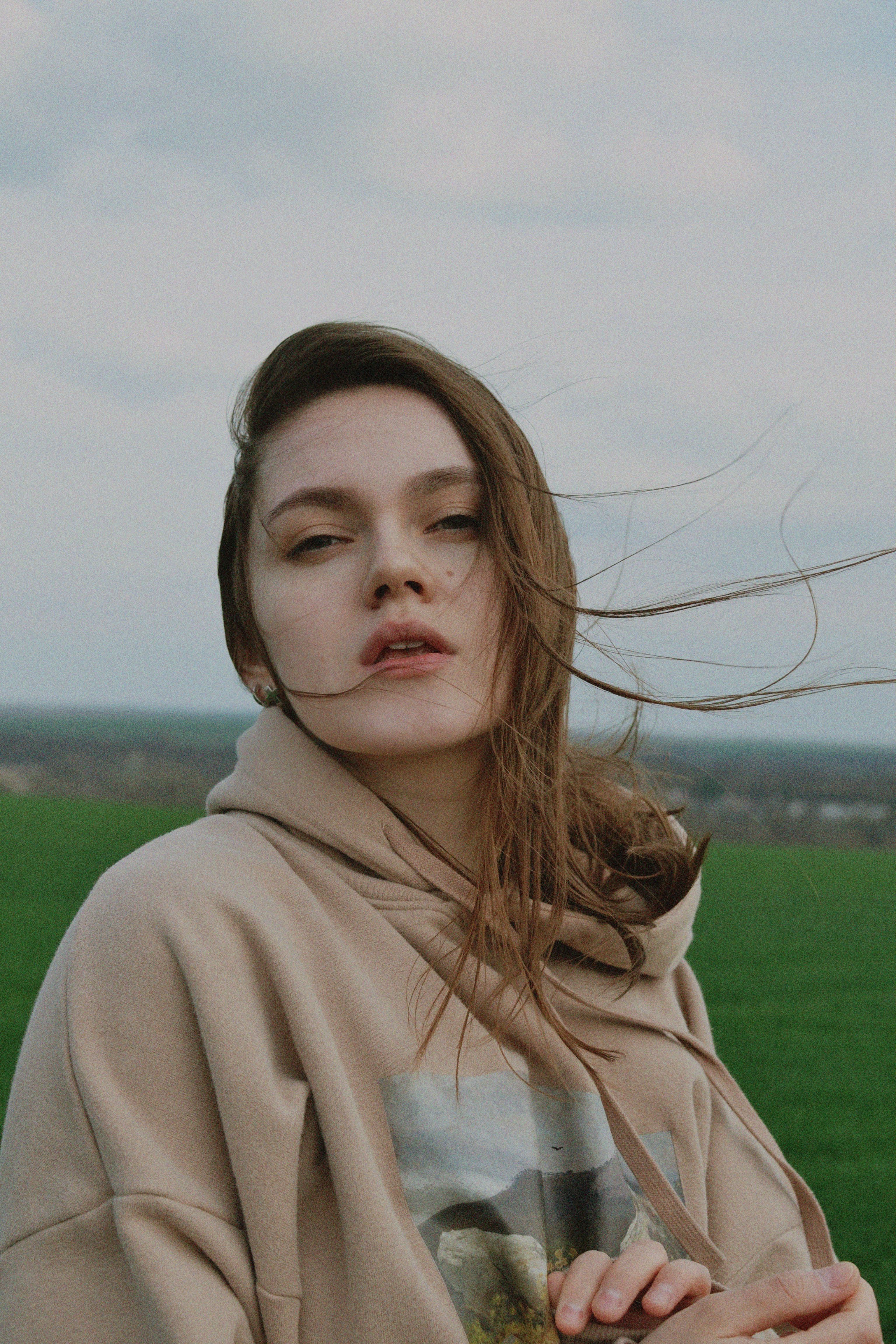 Portrait of a woman standing in a green field with windy hair, wearing a hoodie.