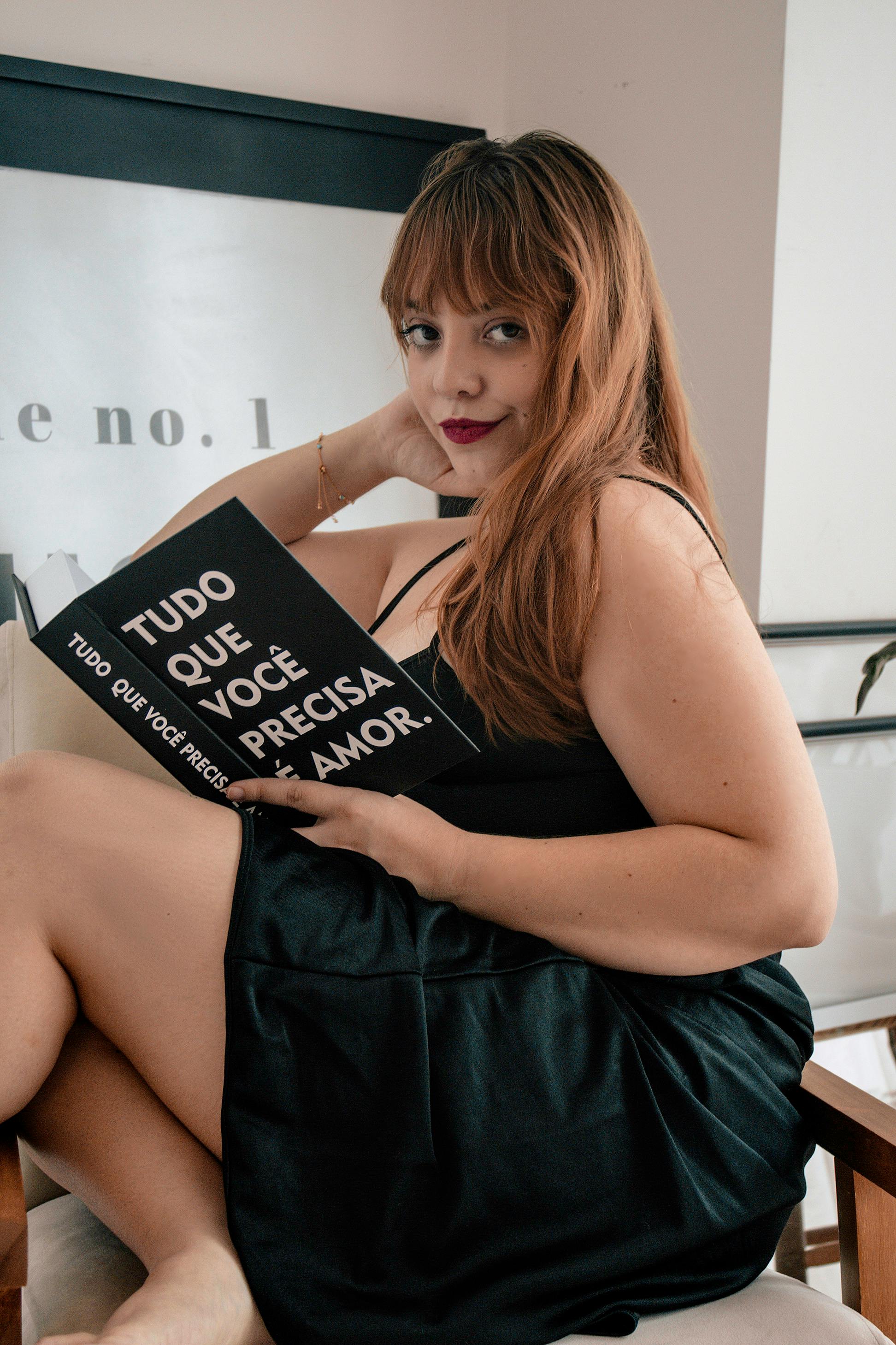 A woman in a stylish dress reads a book indoors, in Curitiba, Brazil.