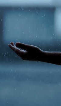 Silhouette of a human hand catching raindrops against a blurred background, creating a serene mood.