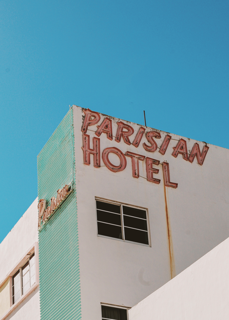 An exterior view of Parisian Hotel with vintage signage against a clear sky in Miami, FL.